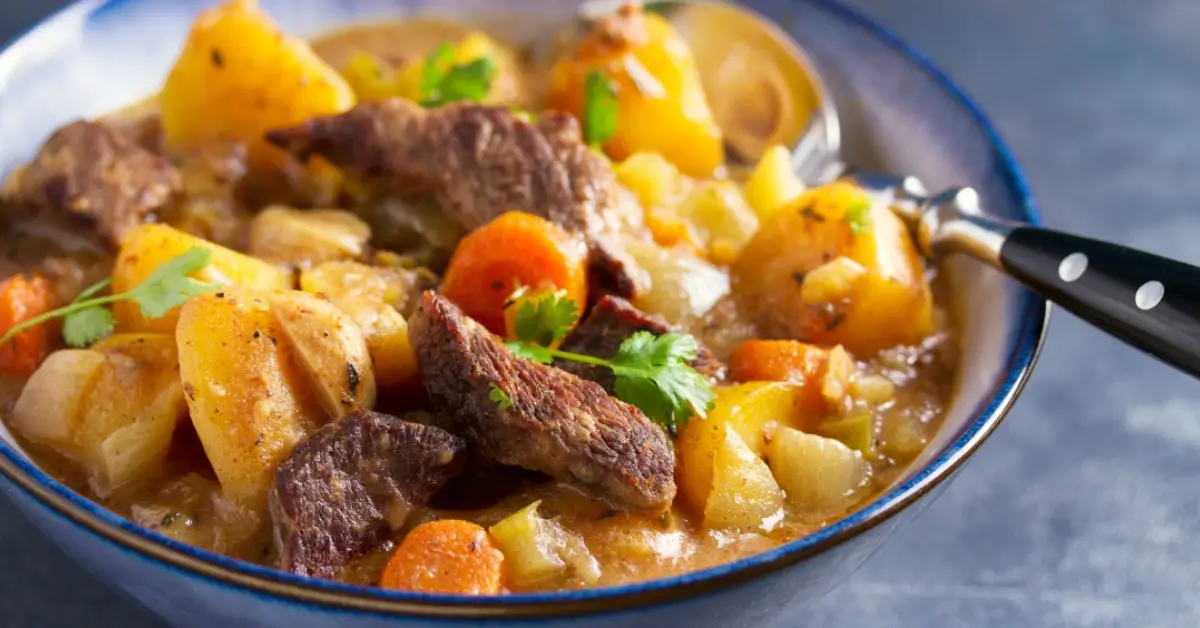 A close-up of a hearty beef stew with carrots, potatoes, and fresh parsley in a black slow cooker.