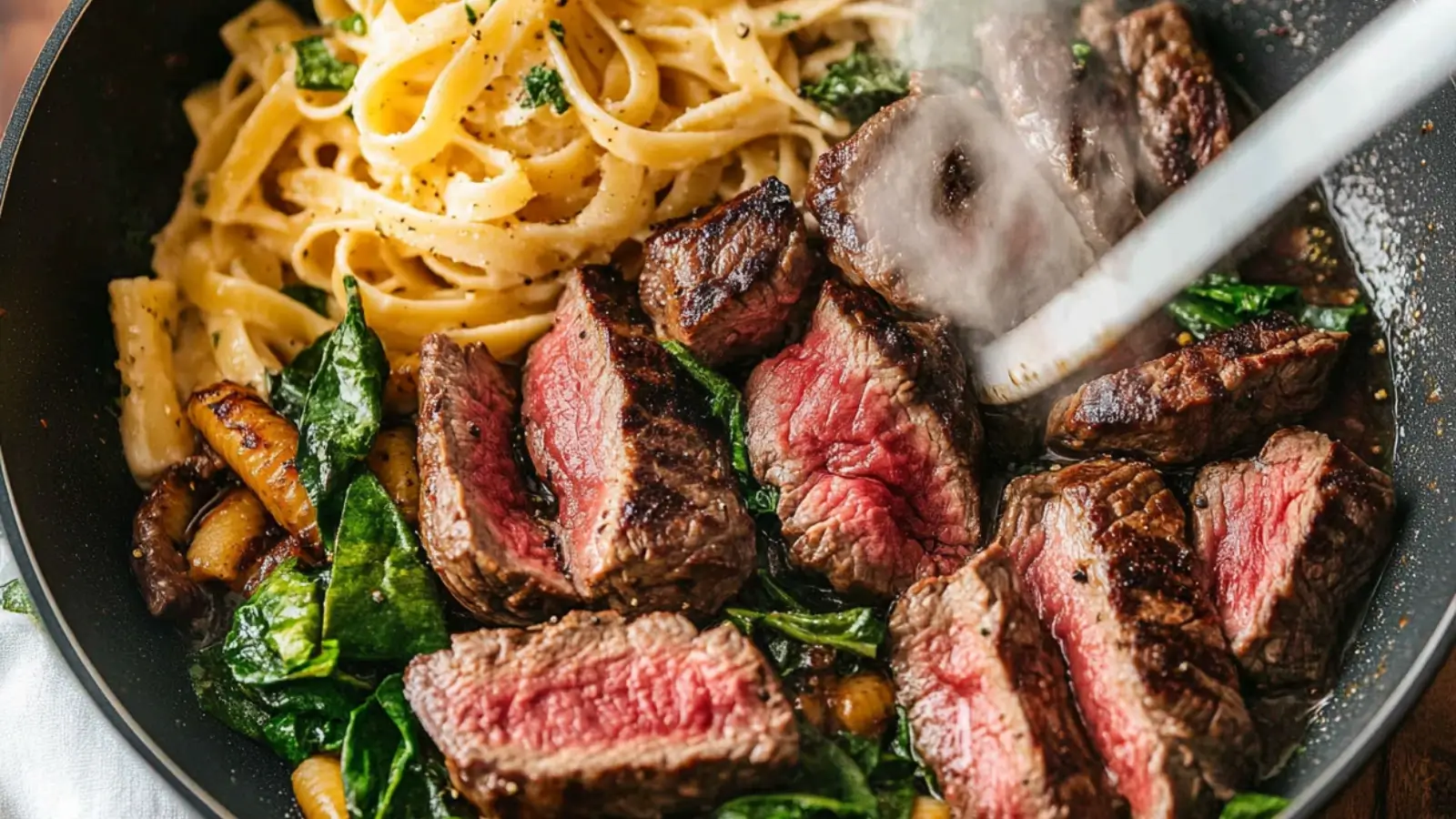 A bowl of steak and pasta, with seared steak slices, golden pasta, and creamy sauce, garnished with Parmesan and herbs.